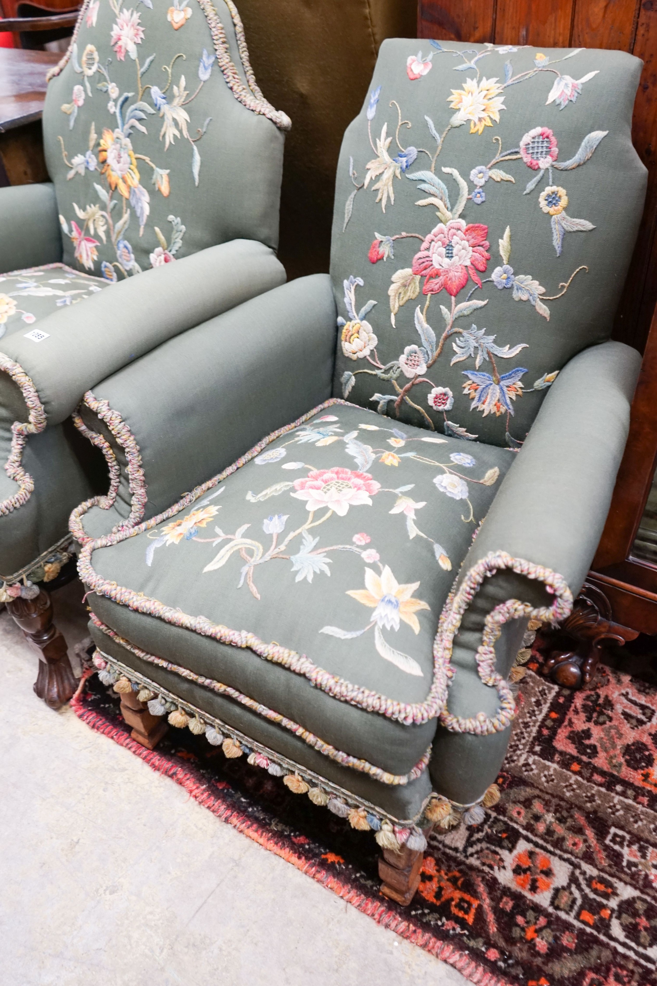 Two armchairs with shaped backs, each upholstered in green with embroidered flowers, on shaped cross stretchers with scrolled feet, larger width 80cm, depth 70cm, height 102cm
